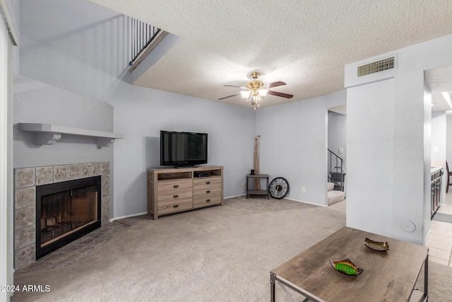 living room with ceiling fan, carpet flooring, visible vents, stairs, and a tiled fireplace