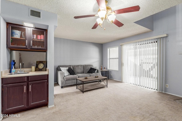 living room featuring light colored carpet, visible vents, ceiling fan, a textured ceiling, and baseboards