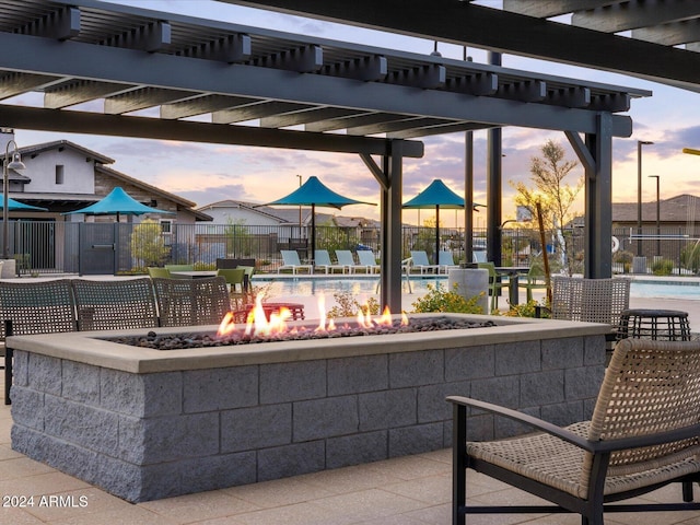 patio terrace at dusk featuring a community pool, a fire pit, and a pergola