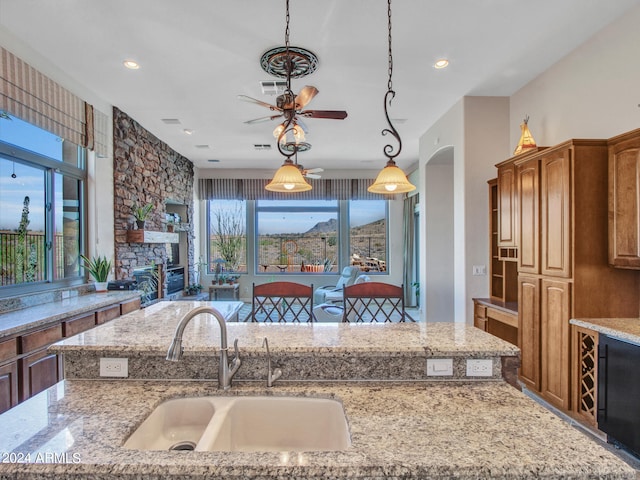 kitchen with light stone counters, a fireplace, pendant lighting, ceiling fan, and sink