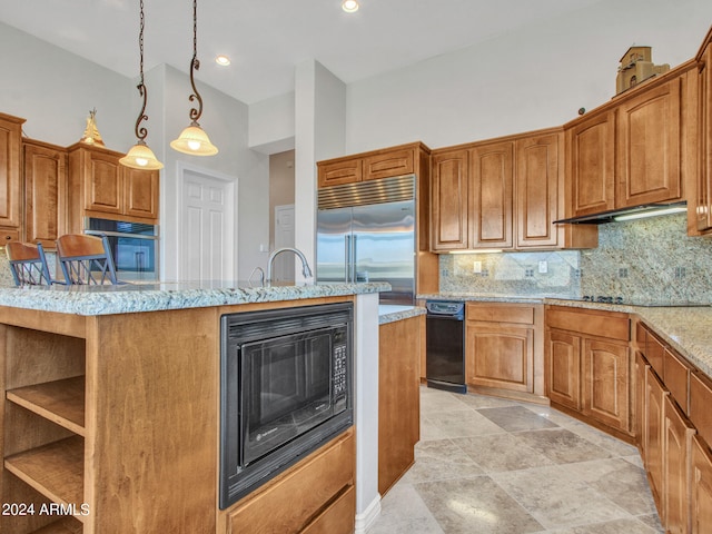 kitchen featuring light stone counters, hanging light fixtures, built in appliances, a kitchen breakfast bar, and decorative backsplash