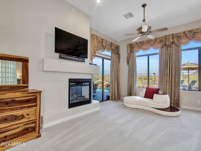 sitting room with ceiling fan, a multi sided fireplace, and carpet flooring