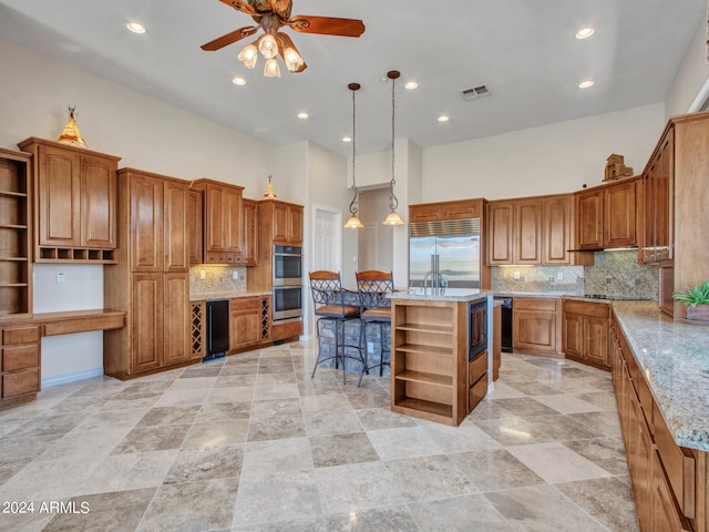 kitchen featuring built in appliances, hanging light fixtures, a kitchen island, a towering ceiling, and ceiling fan