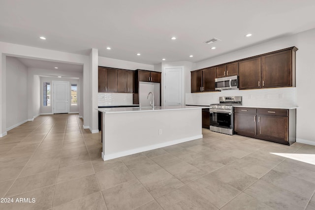 kitchen with stainless steel appliances, tasteful backsplash, dark brown cabinets, and a center island with sink