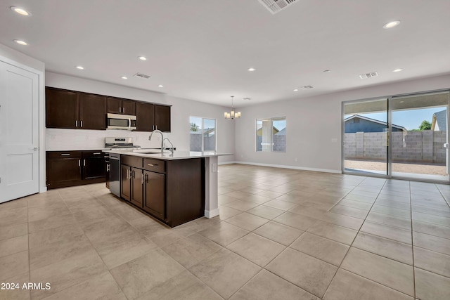 kitchen featuring sink, dark brown cabinets, a notable chandelier, pendant lighting, and a kitchen island with sink