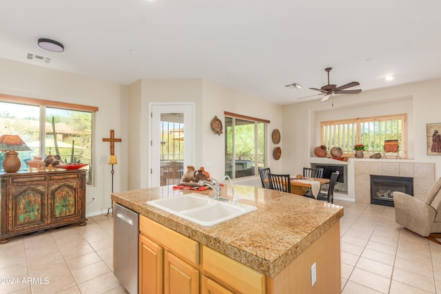 kitchen with sink, a fireplace, stainless steel dishwasher, light tile patterned floors, and a center island with sink
