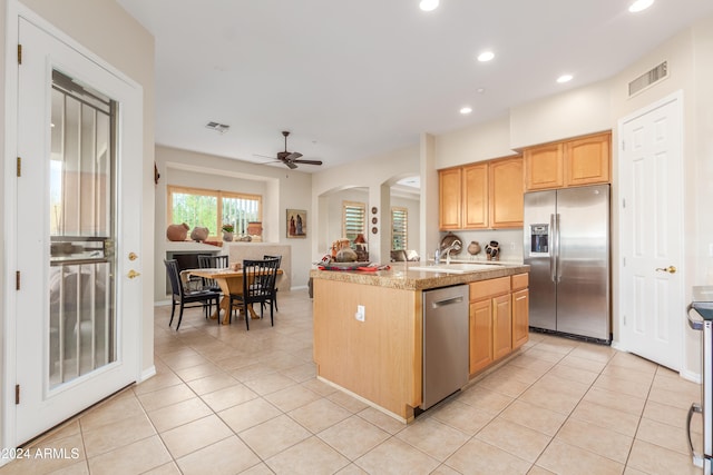 kitchen featuring stainless steel appliances, a center island with sink, sink, light stone counters, and ceiling fan