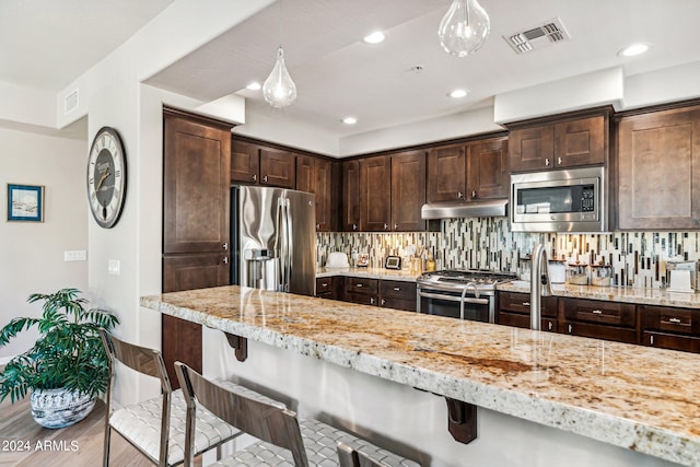 kitchen with appliances with stainless steel finishes, decorative light fixtures, and a kitchen breakfast bar