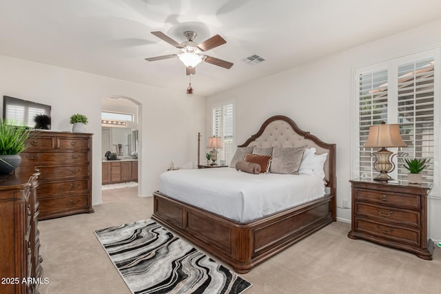 bedroom featuring arched walkways, light carpet, ensuite bath, and visible vents