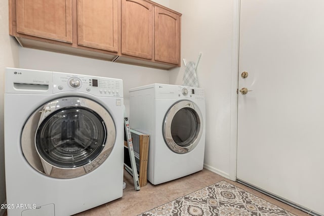 clothes washing area with cabinet space, washing machine and dryer, and light tile patterned floors