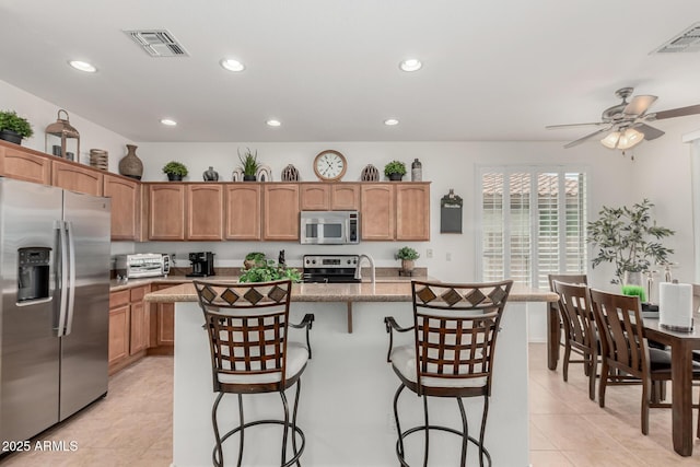 kitchen featuring visible vents, a kitchen island with sink, appliances with stainless steel finishes, and a kitchen breakfast bar