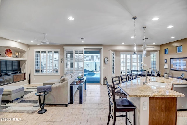 kitchen featuring built in shelves, sink, hanging light fixtures, dishwasher, and light stone countertops