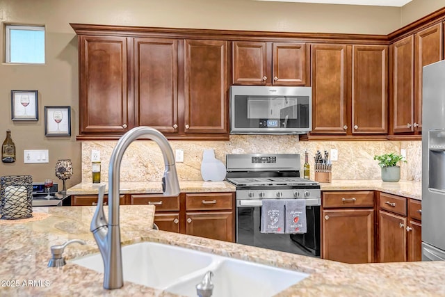 kitchen with tasteful backsplash, appliances with stainless steel finishes, light stone countertops, and sink