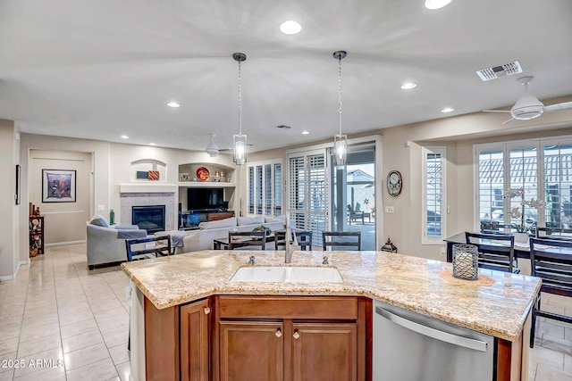 kitchen with an island with sink, sink, stainless steel dishwasher, light stone counters, and built in shelves