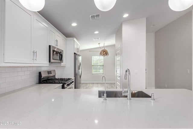 kitchen featuring stainless steel appliances, visible vents, decorative backsplash, white cabinets, and a sink