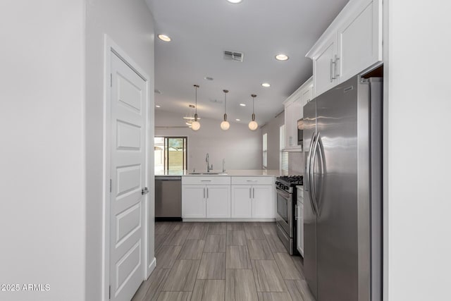 kitchen with white cabinets, stainless steel appliances, a sink, and decorative light fixtures