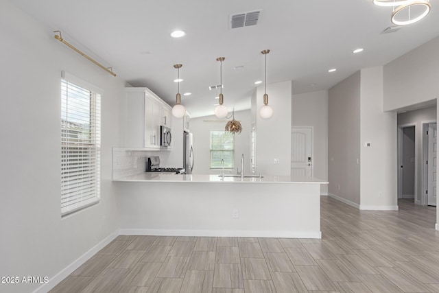 kitchen featuring tasteful backsplash, visible vents, a peninsula, stainless steel appliances, and light countertops