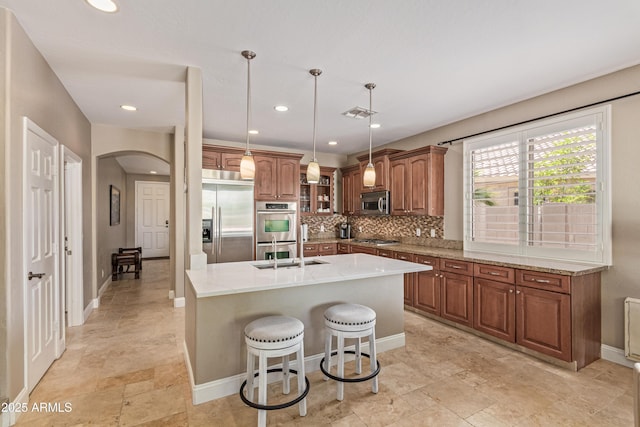 6847 S 27th Pl, Phoenix, AZ 85042 - kitchen featuring stainless steel appliances, arched walkways, brown cabinets, decorative backsplash, and light stone countertops