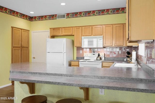 kitchen with light brown cabinetry, a sink, white appliances, a peninsula, and decorative backsplash