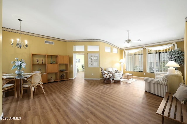 living area featuring visible vents, ceiling fan with notable chandelier, wood finished floors, crown molding, and baseboards