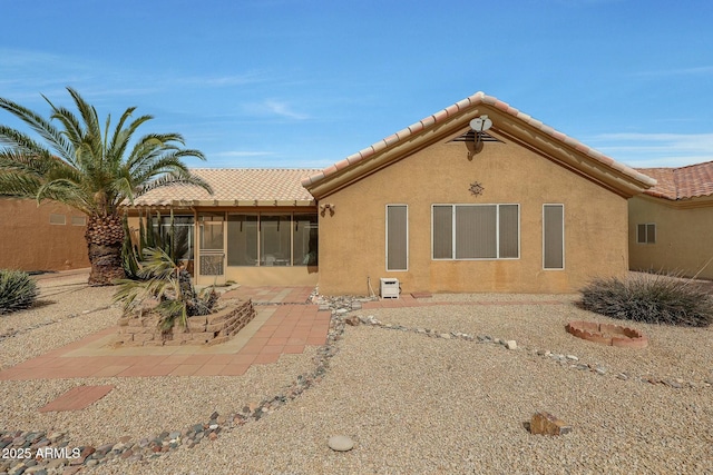 rear view of house featuring stucco siding, a tile roof, and a sunroom