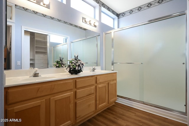 bathroom with double vanity, wood finished floors, a stall shower, and a sink