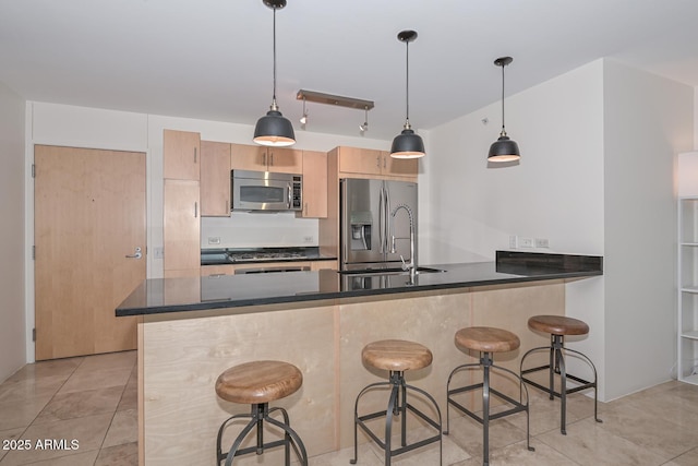 kitchen with light brown cabinets, stainless steel appliances, kitchen peninsula, and hanging light fixtures