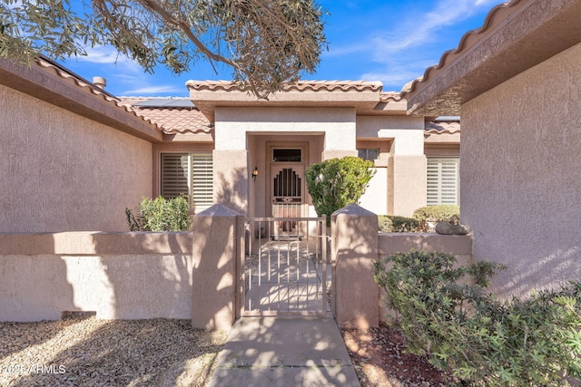 property entrance featuring a gate, a tile roof, roof mounted solar panels, and stucco siding