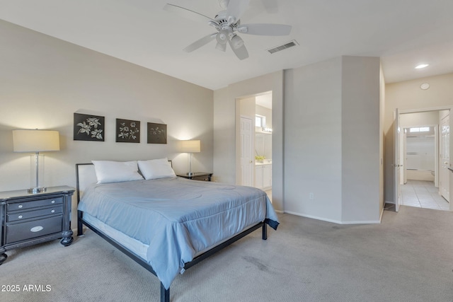 bedroom featuring ceiling fan, light colored carpet, visible vents, baseboards, and ensuite bath