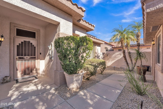 property entrance featuring a tile roof, visible vents, and stucco siding