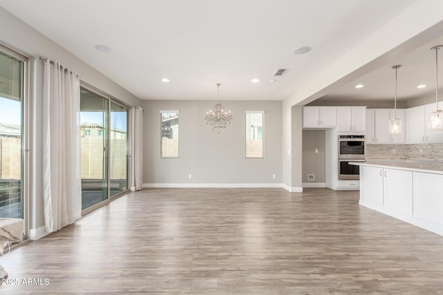 unfurnished living room with an inviting chandelier and light hardwood / wood-style floors