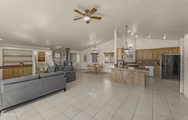 living area featuring a wood stove, light tile patterned floors, ceiling fan with notable chandelier, and vaulted ceiling