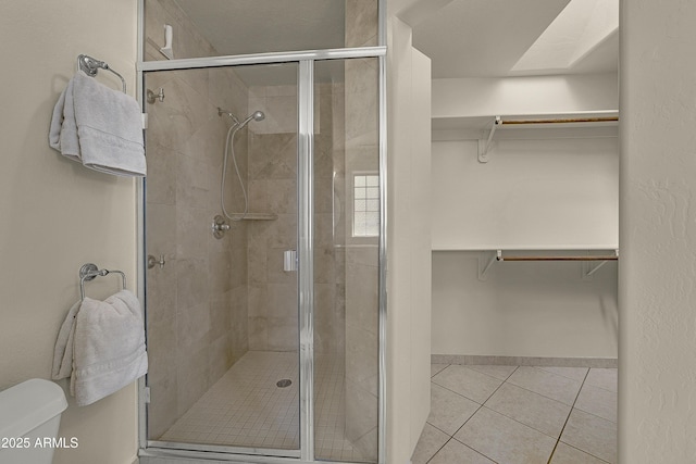bathroom featuring tile patterned floors, a spacious closet, a shower stall, and toilet