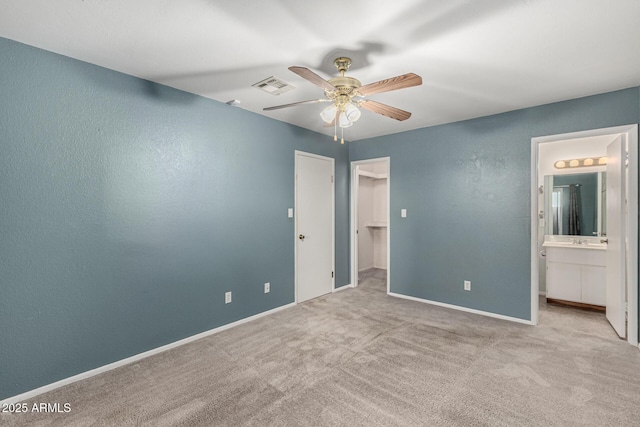 unfurnished bedroom featuring baseboards, visible vents, ensuite bathroom, a walk in closet, and carpet floors