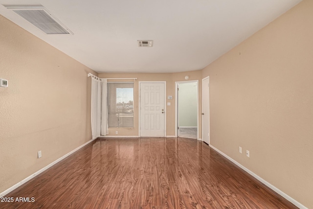 unfurnished room featuring wood finished floors, visible vents, and baseboards