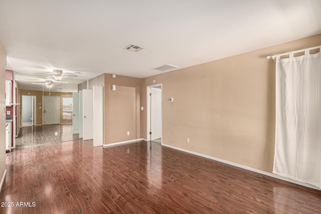 spare room with a ceiling fan, dark wood finished floors, visible vents, and baseboards