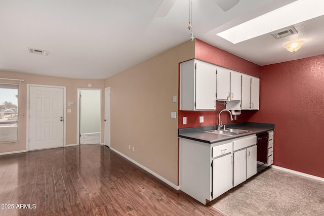 kitchen with a skylight, visible vents, dishwashing machine, wood finished floors, and a sink