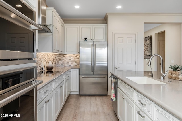 kitchen with sink, ventilation hood, appliances with stainless steel finishes, white cabinets, and backsplash