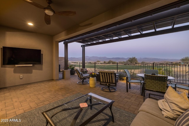 patio terrace at dusk featuring an outdoor living space, a mountain view, ceiling fan, and a pergola