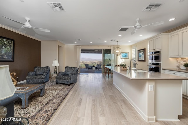 kitchen with light hardwood / wood-style floors, a center island with sink, ceiling fan, and stainless steel double oven