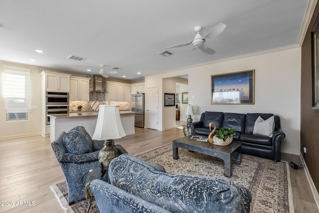 living room featuring ceiling fan, ornamental molding, and light wood-type flooring