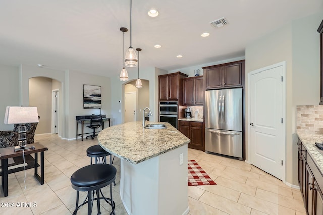 kitchen with decorative backsplash, light stone countertops, appliances with stainless steel finishes, and a kitchen island with sink