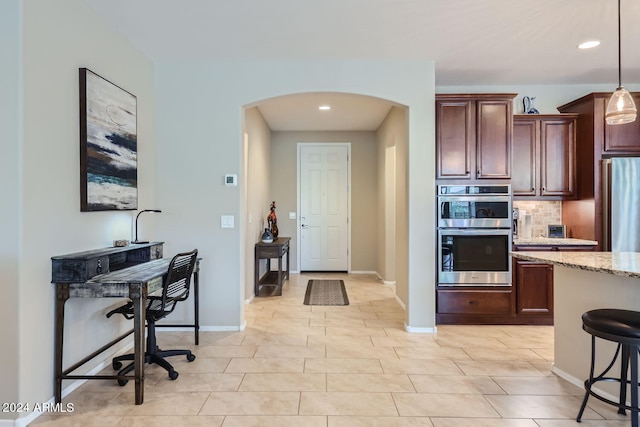 kitchen featuring pendant lighting, tasteful backsplash, appliances with stainless steel finishes, a breakfast bar, and light stone countertops