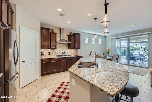 kitchen featuring an island with sink, hanging light fixtures, sink, wall chimney range hood, and stainless steel appliances