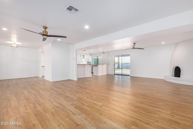 unfurnished living room featuring a large fireplace, ceiling fan, and light wood-type flooring