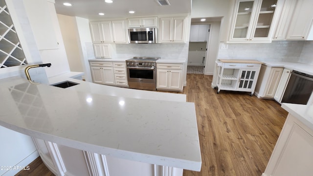 kitchen featuring white cabinetry, light hardwood / wood-style floors, kitchen peninsula, backsplash, and appliances with stainless steel finishes