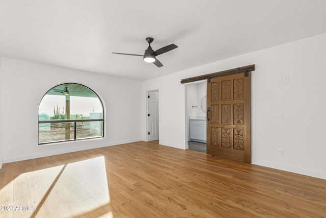 spare room featuring ceiling fan, a barn door, and wood-type flooring