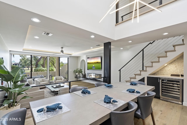 dining room featuring a raised ceiling, wine cooler, a wall of windows, light wood-type flooring, and ceiling fan