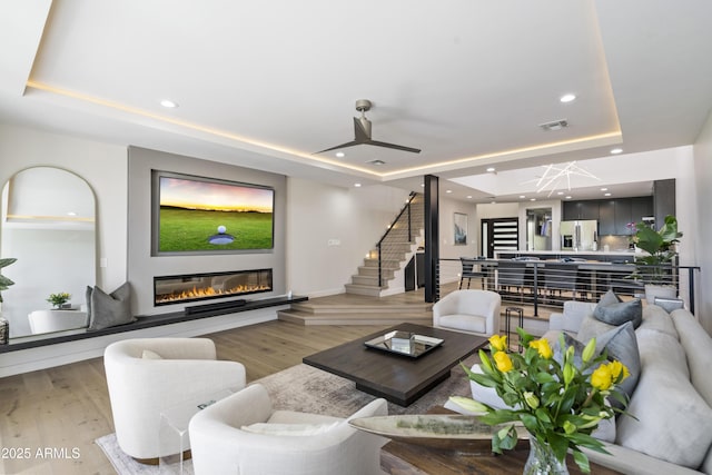 living room with hardwood / wood-style floors, a raised ceiling, and ceiling fan