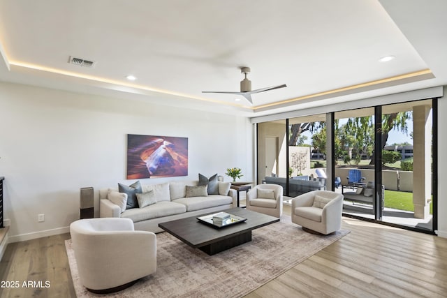 living room featuring floor to ceiling windows, a raised ceiling, ceiling fan, and light hardwood / wood-style floors